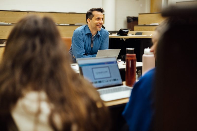 Steve Matuszak, wearing a blue shirt and sitting behind a laptop, talks to students in a Pamplin classroom.
