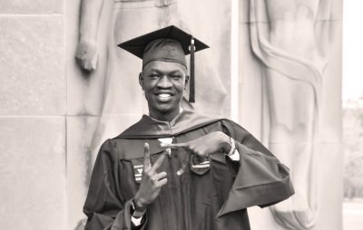 Dudi Miabok, wearing a cap and gown, makes the VT symbol with his hands in front of the Pylons