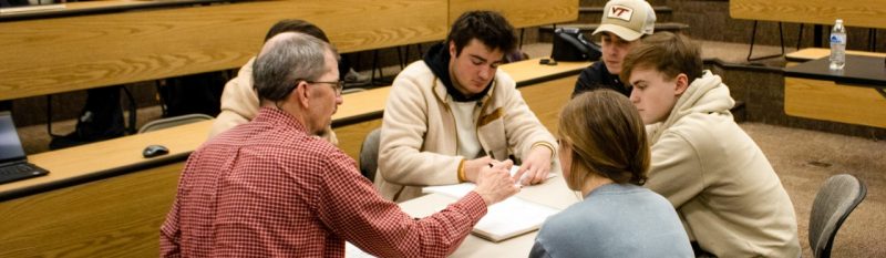 A professor sits with students to work on resumes.